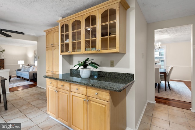 kitchen featuring light tile patterned flooring, ceiling fan, glass insert cabinets, light brown cabinets, and a textured ceiling