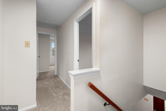 hall with an upstairs landing, light colored carpet, attic access, and baseboards