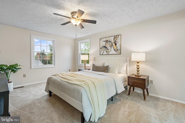bedroom featuring light carpet, a textured ceiling, baseboards, and a ceiling fan