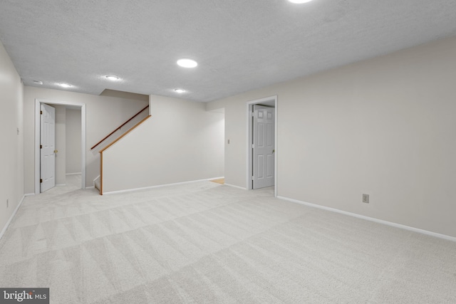 finished basement featuring a textured ceiling, light colored carpet, baseboards, stairs, and recessed lighting