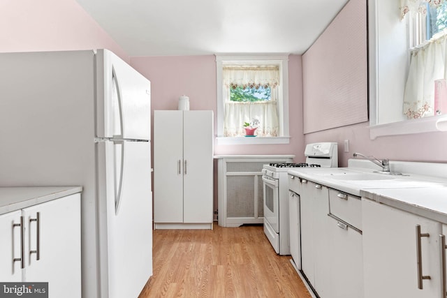 kitchen featuring white appliances, a sink, light wood-style flooring, light countertops, and white cabinetry