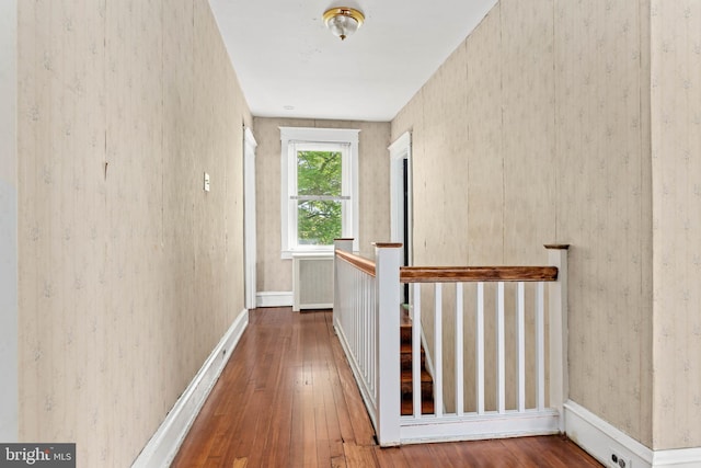 hallway with wallpapered walls, an upstairs landing, hardwood / wood-style floors, and baseboards