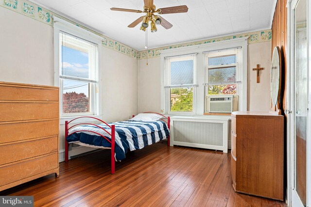 bedroom with radiator, hardwood / wood-style floors, multiple windows, and cooling unit