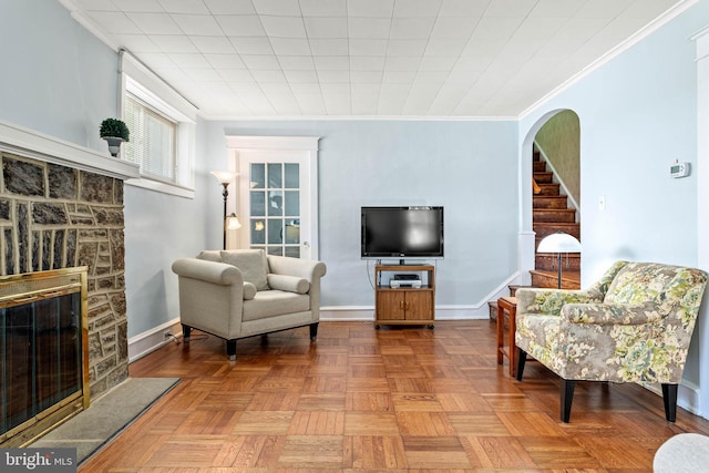 living area featuring a fireplace, stairway, baseboards, arched walkways, and ornamental molding