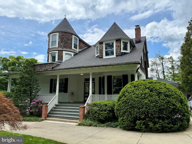 view of front of house featuring a chimney, covered porch, and a shingled roof