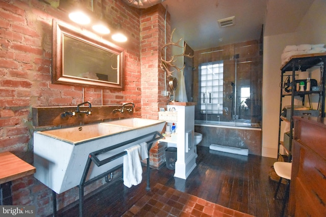 1830 Columbia Rd NW, Washington, DC 20009 - bathroom featuring toilet, combined bath / shower with glass door, wood-type flooring, brick wall, and visible vents