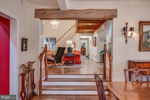 stairway featuring beam ceiling, hardwood / wood-style flooring, and a chandelier