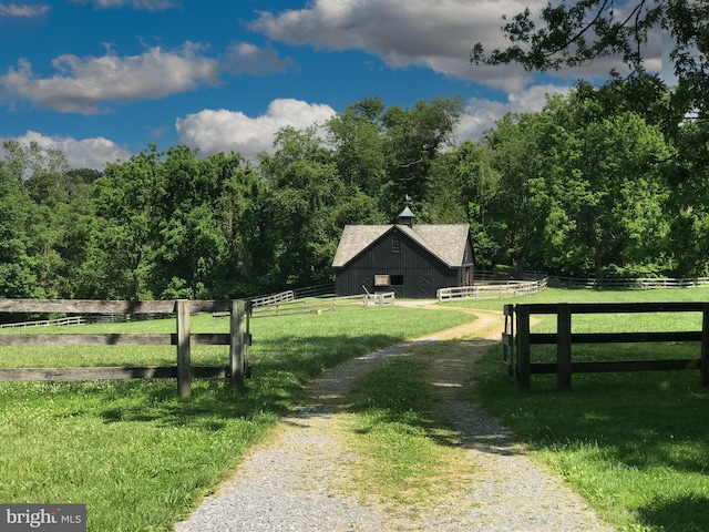 view of dirt / gravel road featuring a view of trees, a barn, and a view of countryside