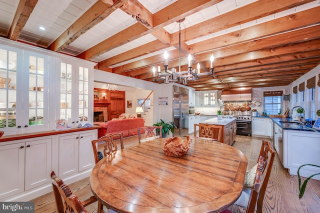 dining space with light wood-style flooring, a chandelier, and beam ceiling