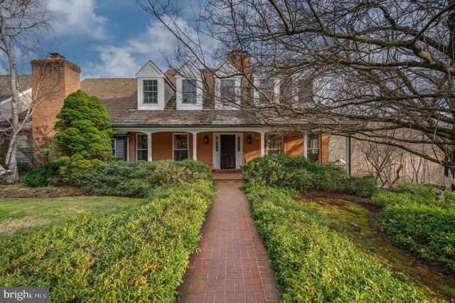 view of front of home featuring a chimney, a porch, and brick siding