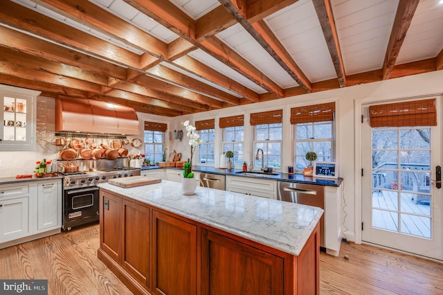 kitchen with exhaust hood, a sink, appliances with stainless steel finishes, light wood-type flooring, and beamed ceiling