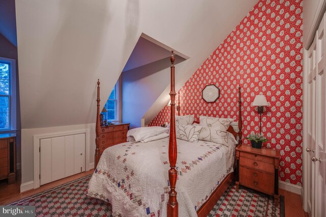bedroom featuring wallpapered walls, baseboards, wood finished floors, and vaulted ceiling