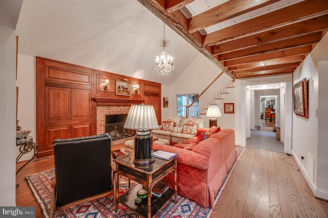 living area featuring stairs, light wood-type flooring, a fireplace, beamed ceiling, and a chandelier