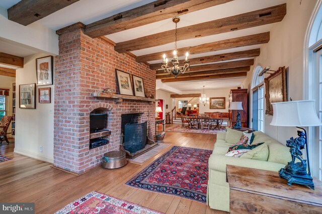 living area featuring a chandelier, hardwood / wood-style floors, beamed ceiling, and a fireplace