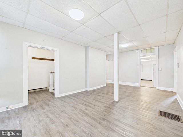 finished basement featuring a drop ceiling, wood finished floors, a baseboard heating unit, and baseboards