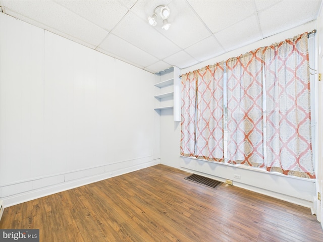spare room with a paneled ceiling, wood finished floors, and baseboards