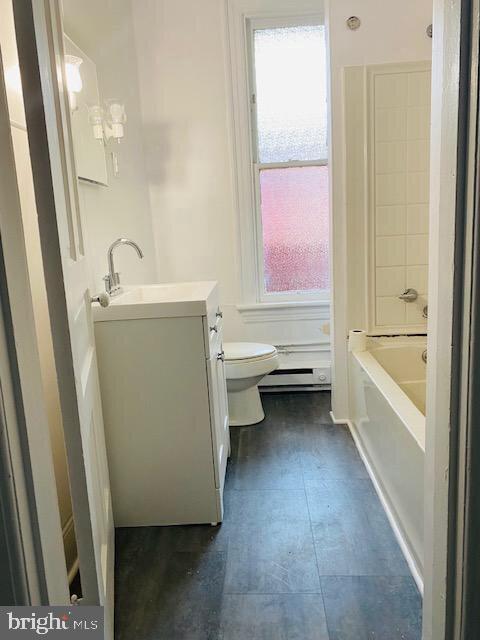 full bath with plenty of natural light, toilet, vanity, and a baseboard heating unit