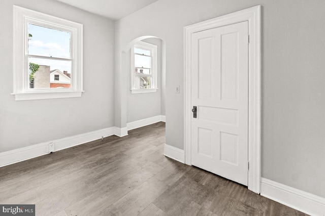 unfurnished bedroom featuring arched walkways, baseboards, and wood finished floors