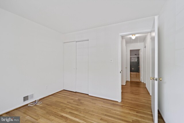 unfurnished bedroom featuring light wood finished floors, a closet, attic access, and baseboards