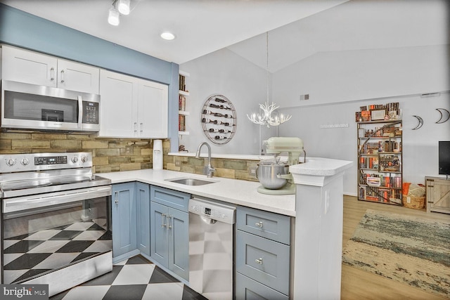 kitchen featuring stainless steel appliances, a sink, a peninsula, light countertops, and white cabinets