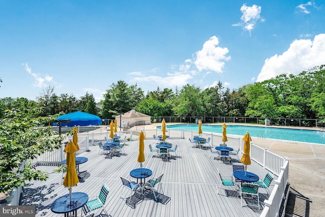 community pool with outdoor dining area, fence, a deck, and view of wooded area
