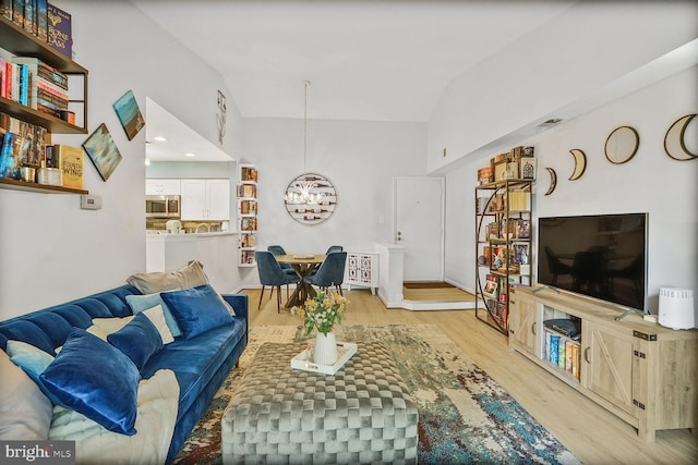 living area featuring a chandelier, light wood finished floors, and vaulted ceiling