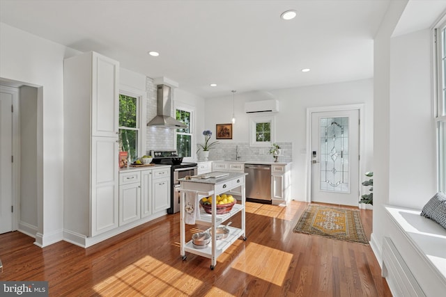kitchen featuring wall chimney range hood, appliances with stainless steel finishes, a wall mounted air conditioner, decorative backsplash, and light countertops