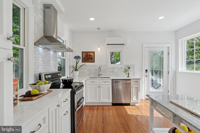 kitchen featuring appliances with stainless steel finishes, a sink, exhaust hood, a wall mounted air conditioner, and decorative backsplash