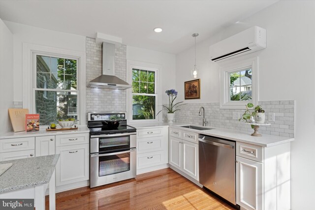 kitchen with wall chimney exhaust hood, stainless steel appliances, a sink, a wall mounted AC, and backsplash