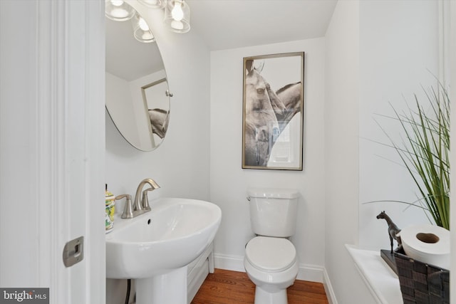 half bathroom featuring baseboards, wood finished floors, a sink, and toilet