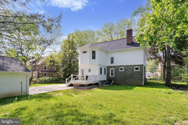 rear view of property with a wooden deck, a chimney, a yard, stucco siding, and stone siding