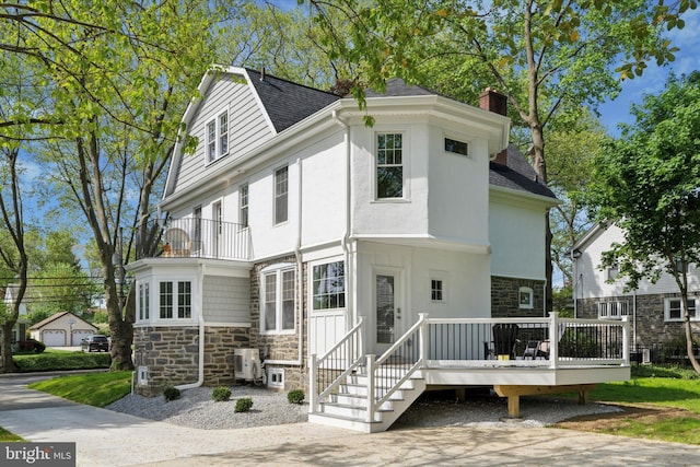view of front of home featuring stone siding, a shingled roof, a balcony, a chimney, and a wooden deck