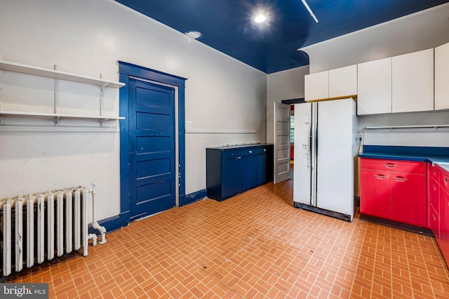kitchen featuring radiator heating unit, freestanding refrigerator, brick patterned flooring, white cabinets, and open shelves