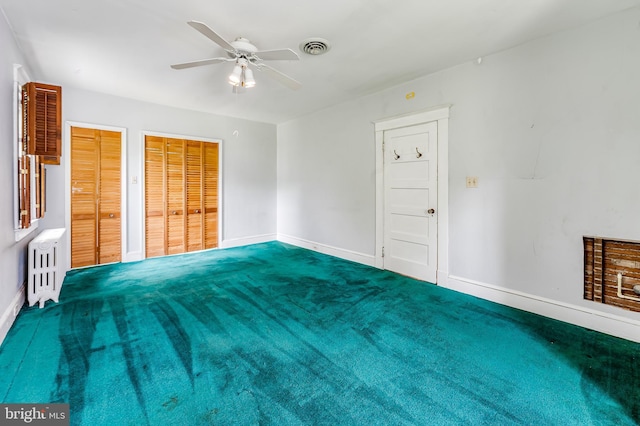 unfurnished bedroom featuring radiator heating unit, baseboards, two closets, a ceiling fan, and carpet floors