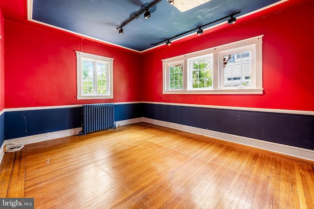 empty room with radiator heating unit, track lighting, healthy amount of natural light, and hardwood / wood-style floors