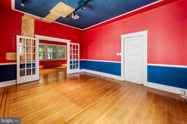 unfurnished room featuring french doors, radiator heating unit, hardwood / wood-style flooring, rail lighting, and baseboards