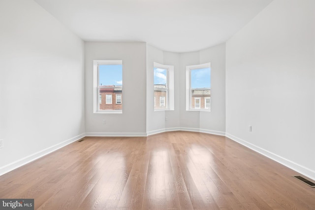 unfurnished room with light wood finished floors, a wealth of natural light, visible vents, and baseboards