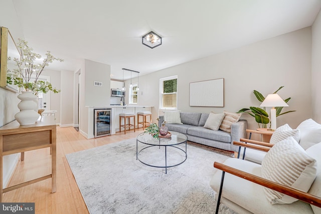 living area featuring beverage cooler, light wood-type flooring, and baseboards