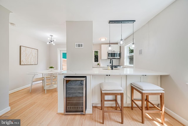 kitchen featuring beverage cooler, stainless steel microwave, light wood-type flooring, baseboards, and backsplash