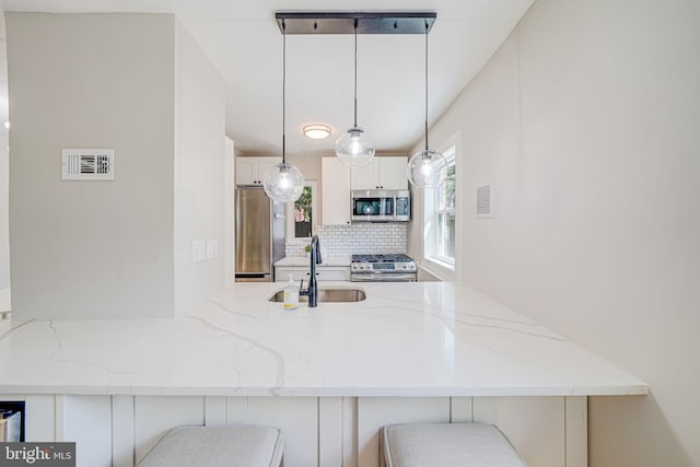 kitchen with appliances with stainless steel finishes, a sink, tasteful backsplash, a breakfast bar area, and light stone counters