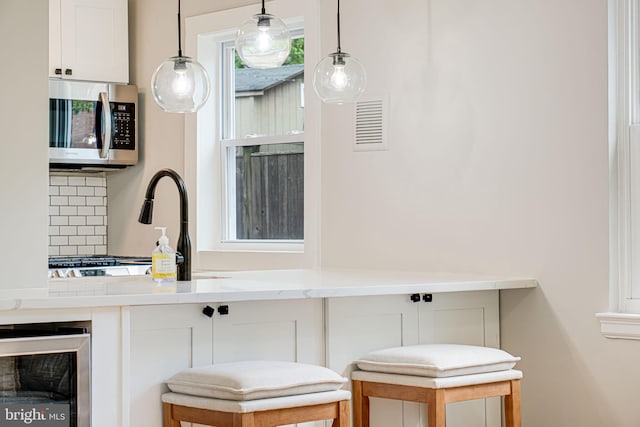 bar with stainless steel microwave, wine cooler, pendant lighting, and decorative backsplash