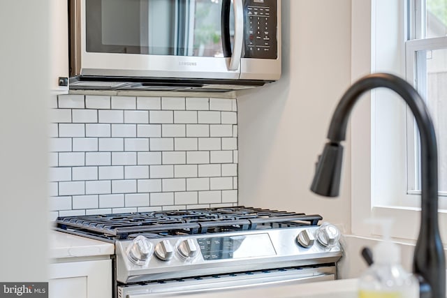 kitchen view of appliances with stainless steel finishes, backsplash, white cabinetry, and light stone countertops