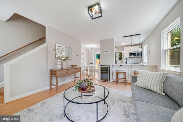 living area featuring wine cooler, light wood-type flooring, baseboards, and stairs