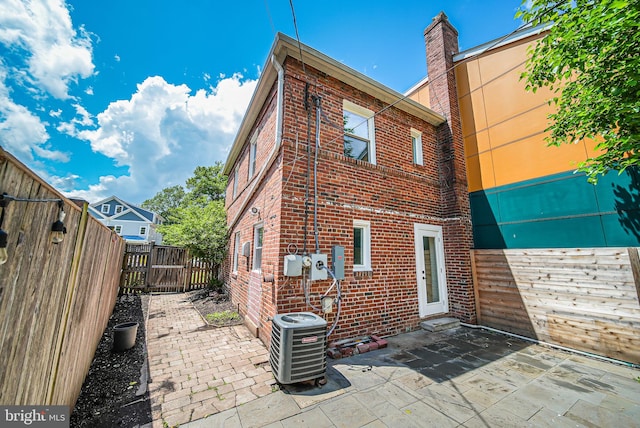 rear view of property featuring brick siding, cooling unit, a fenced backyard, and a patio area
