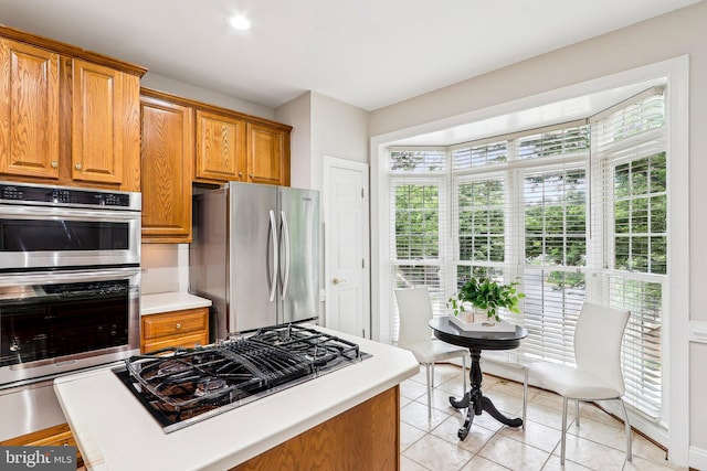 kitchen featuring stainless steel appliances, light tile patterned floors, light countertops, and brown cabinetry