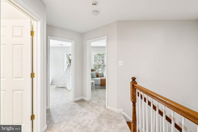 hallway with an upstairs landing, light colored carpet, and baseboards