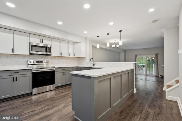 kitchen with appliances with stainless steel finishes, gray cabinetry, a peninsula, dark wood-style flooring, and tasteful backsplash