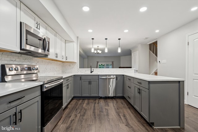 kitchen featuring appliances with stainless steel finishes, gray cabinetry, a peninsula, a sink, and dark wood finished floors