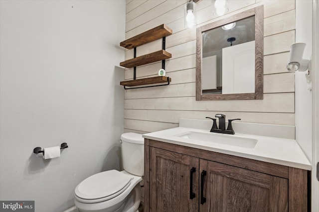 bathroom featuring wood walls, toilet, and vanity