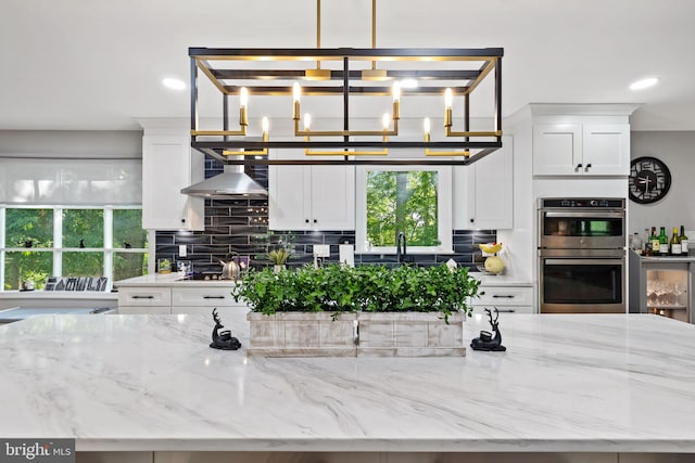 15807 Marlington Dr, Dumfries, VA 22025 - kitchen with light stone countertops, stainless steel double oven, white cabinets, wall chimney range hood, and tasteful backsplash